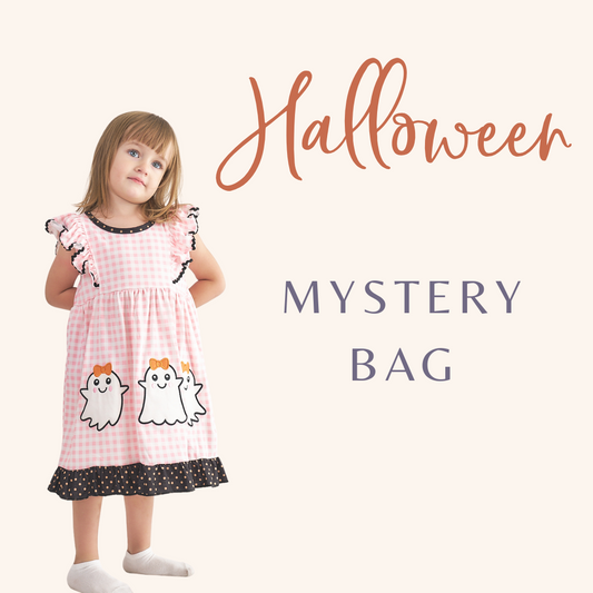 A young child wearing a pink dress with a Halloween theme, including two white ghosts, standing against a white background with the text 'Halloween' and 'MYSTERY BAG' added visually.